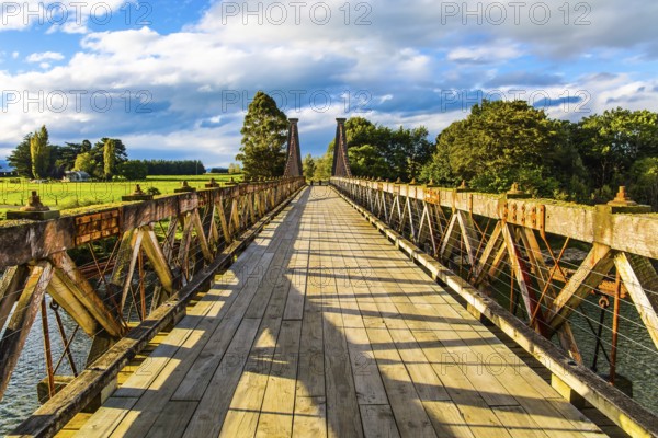 Wooden suspension bridge over a quiet river. South Island, New Zealand. Incredible cloudy sunset. Southern Scenic Route. The concept of eco and photo tourism