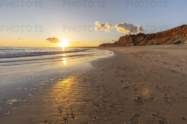 Beautiful sandy beach with red rocks and cliffs. Twilight at sunset with shallow waves on the Atlantic coast in Praia do Poço Velho, Praia da Falésia, Algarve, Portugal, Europe