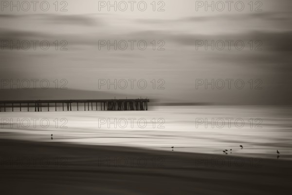 The smooth water of the Pacific with mountain silhouettes on the horizon and a wooden jetty