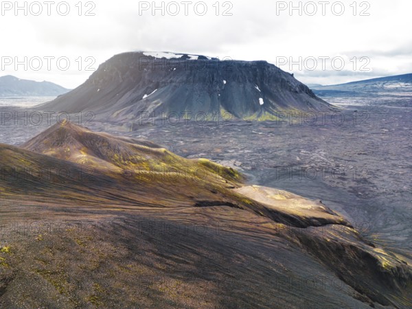 Remote volcanic lands somewhere in Iceland mainland, surrounded by vibrant green bushes and volcanic lands. Volcanic rock formations, small mountains, black grey volcanic rock. No people