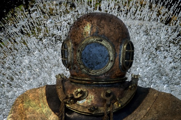 Metal diving helmet with round viewing windows amidst swirling air bubbles. Landscape format. Diving helmet made of metal with round viewing windows amid swirling air bubbles. Horizontal format