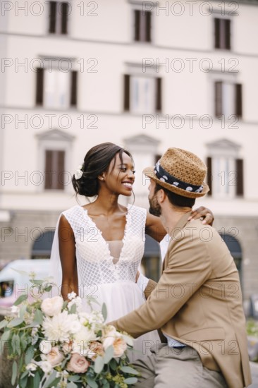 Multiracial wedding couple. Wedding in Florence, Italy. African-American bride in a white dress with a long veil and a bouquet, and Caucasian groom in a sandy jacket and straw hat