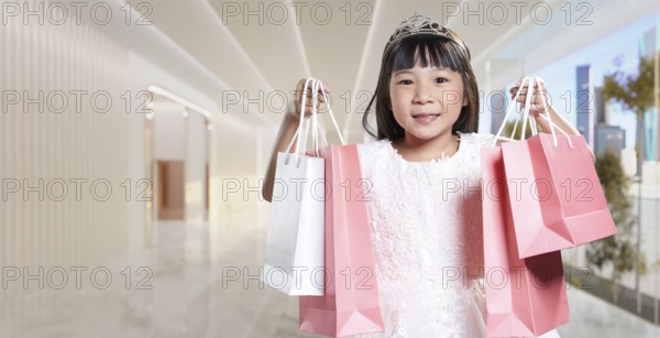 Asian girl wearing a princess tiara is smiling and holding shopping bags inside of a mall