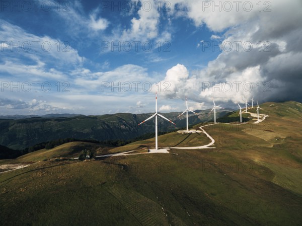 The prospect of a number of high industrial wind turbines on the hill, against the blue sky and velvet white clouds.