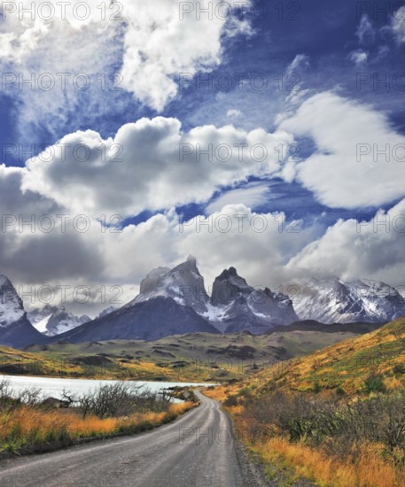 Picturesque clouds piled up in the blue sky. The gravel road goes to the famous cliffs of Los Kuernos. Windy day in the Chilean Patagonia