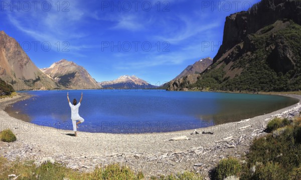 Yoga on the lake. Mature woman in white performs asana tree, standing on the shore of round lake