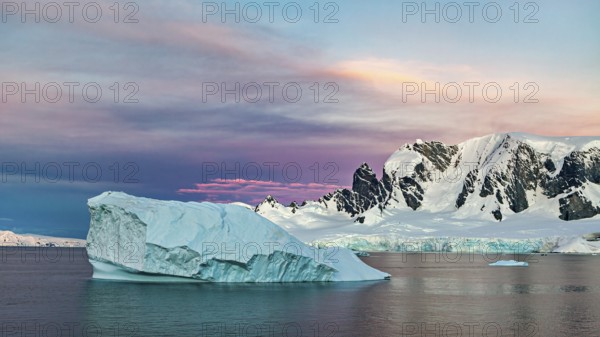 Iceberg floating in the sea in front of a snow-covered mountain backdrop at sunset, icebergs in the Southern Ocean in Antarctica