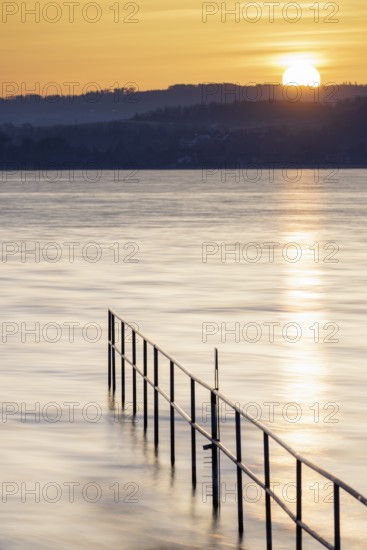 Rising sun over calm lake, railing extends into the water, lido, Litzelstetten, Lake Constance, Baden-Württemberg, Germany, Europe