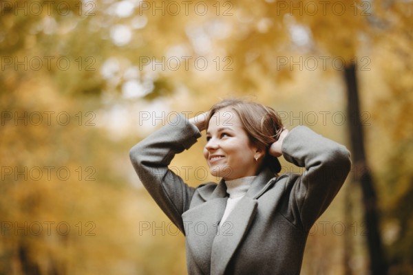 A woman smiling in a coat with autumn leaves in the background