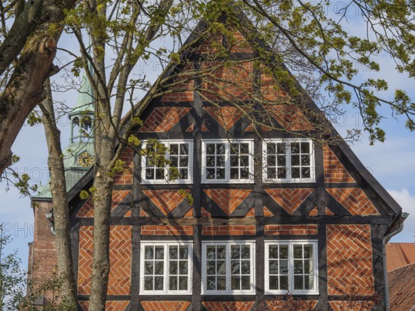 The picture shows a half-timbered house with red bricks, surrounded by trees. A church spire is visible in the background, lüneburg, germany