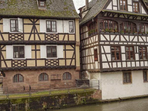 Two historic half-timbered houses side by side along a canal on a rainy day, strasbourg, france