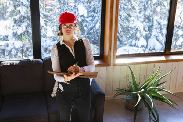 Worker woman at work concept. female home inspector wearing a red hard hat takes professional notes on her clipboard during air quality inspection