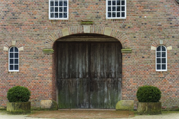 Large wooden gate in a symmetrical brick building with trimmed shrubs, vreden, münsterland, North Rhine-Westphalia, germany