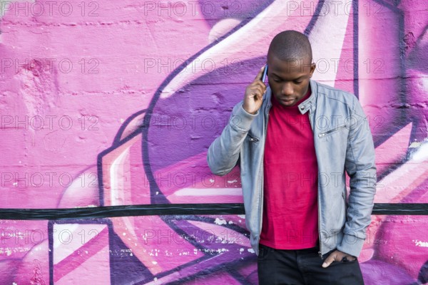 Portrait of a hot black man in front of graffiti wall, using cell phone, posing for camera