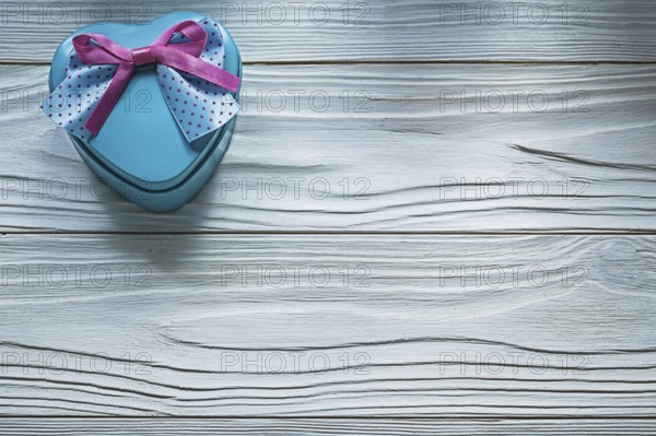 Heart-shaped blue present box with pink bow on wooden board holidays concept