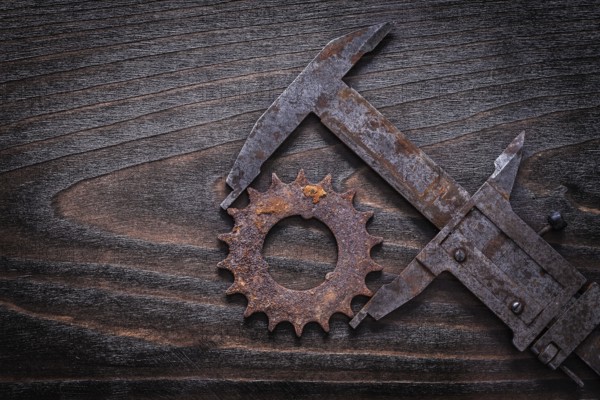 Rusty retro-styled measuring calipers with pinion gear on vintage dark wooden background construction concept