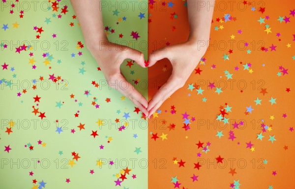 Top view of anonymous female with hands in shape of heart on two colored background with confetti stars