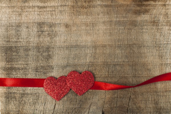 Red ribbon tape and hearts on wooden background