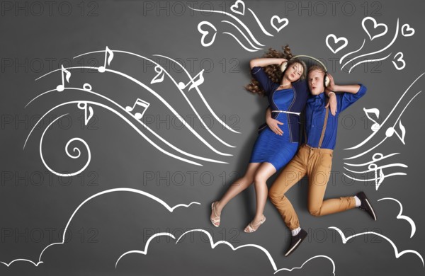 Happy valentines love story concept of a romantic couple sharing headphones and listening to music against chalk drawings background of notes, player icons and clouds