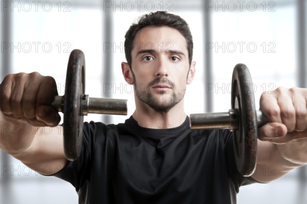 Personal Trainer doing front dumbell raises for training his deltoids in a brown background