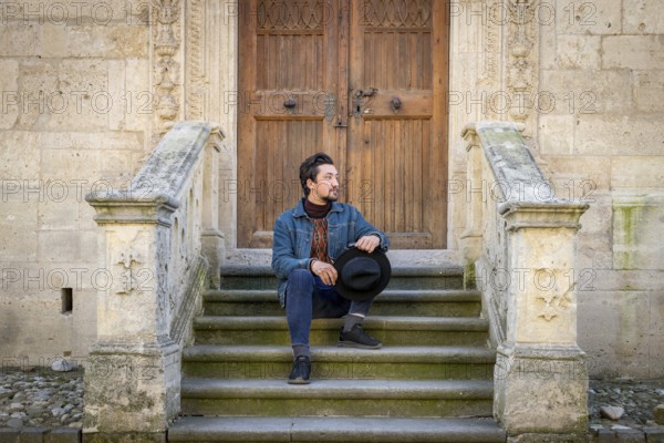 Portrait of a young man sitting against a beautiful old medieval cathedral door. A man in front of a an old architecture church entrance door in Alba Iulia, Romania, Europe