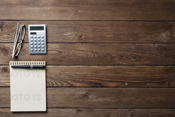 Still life of accountant workspace with office accessories. Flat lay wooden desk with elegant glasses, calculator and spiral notepad. Accounting and banking services. Finance and investment concept