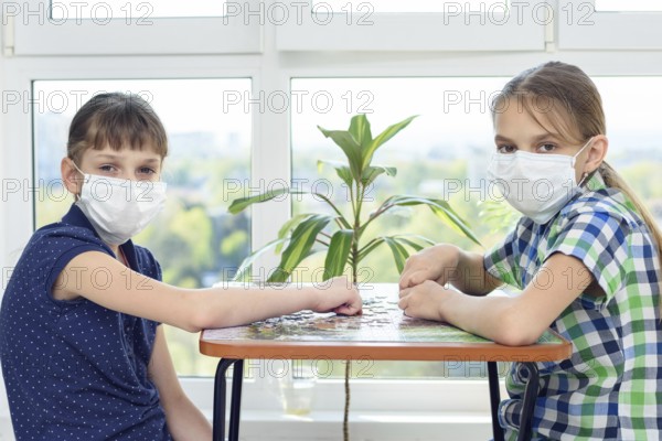 Two girlfriends in medical masks play puzzles and looked into the frame