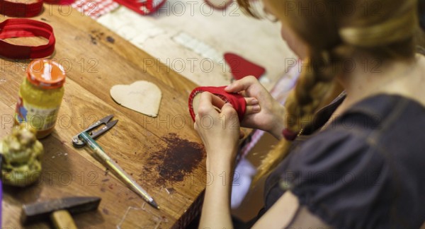 Brown-haired woman manufacturing heart-shaped red purses on the wooden table