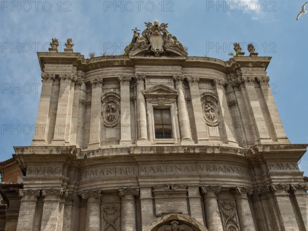 Front façade of a baroque building with intricate ornamentation and Latin inscription, framed in a blue sky, Rome, Italy, Europe