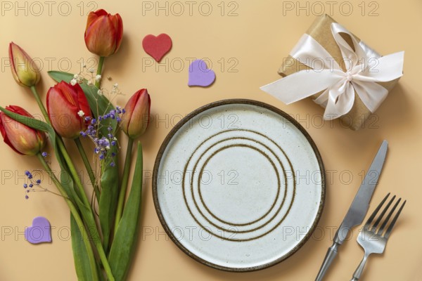 Beautiful table setting with gift box, decorative hearts and tulips flowers on pastel peach background. Happy Mother's day concept background 2024. View from above. Empty space for text