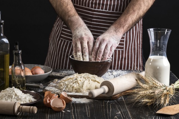A handful of flour with egg on a rustic kitchen. Against the background of men's hands knead the dough. Ingredients for cooking flour products or dough bread, muffins, pie, pizza dough . Copy space