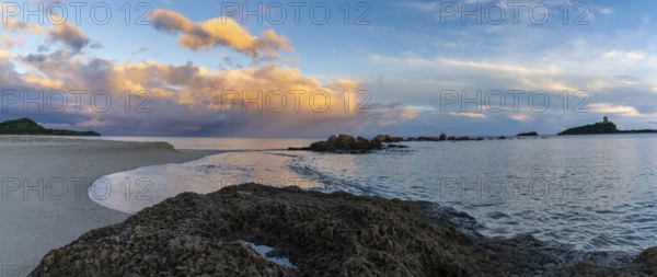 A panorama view of a colorful sunset at Nora Beach in Sardinia with the Coltellazzo Tower in the background