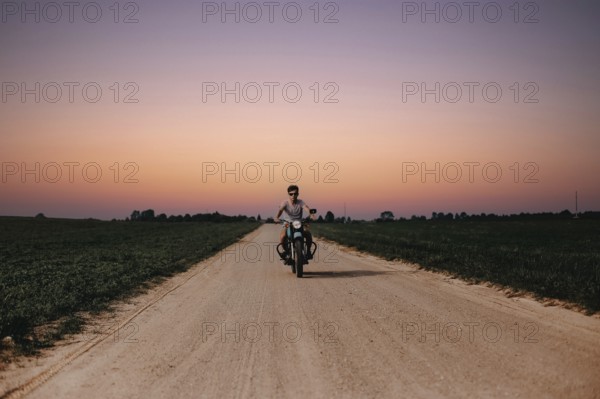 Rider on a motorcycle advances along a rural road during sunset, creating a serene atmosphere