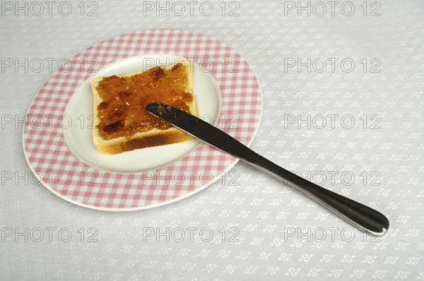 Spread jam on bread with knife. Pink checkered plate