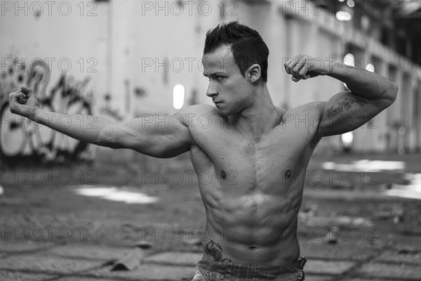 Muscular shirtless young man in abandoned warehouse standing, striking cool pose