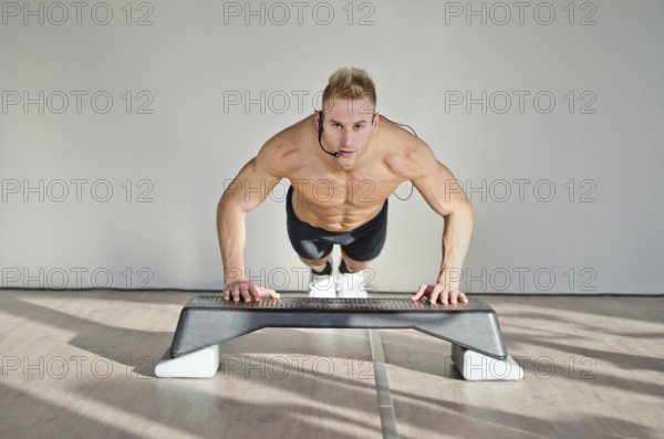 Young aerobics male coach shirtless leaning on step teaching class