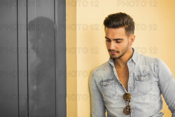 Attractive young man standing against colorful wall, looking to a side, wearing denim shirt
