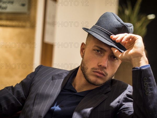 Handsome elegant man in hotel or night club lounge, wearing business suit and fedora hat, looking at camera