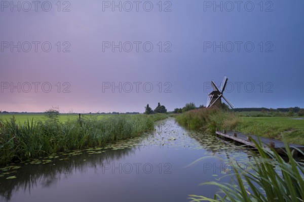 Charming windmill by river at rainy sunrise, Holland