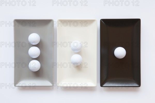 Different ceramic dishes with golf balls on over white background, rectangle dish