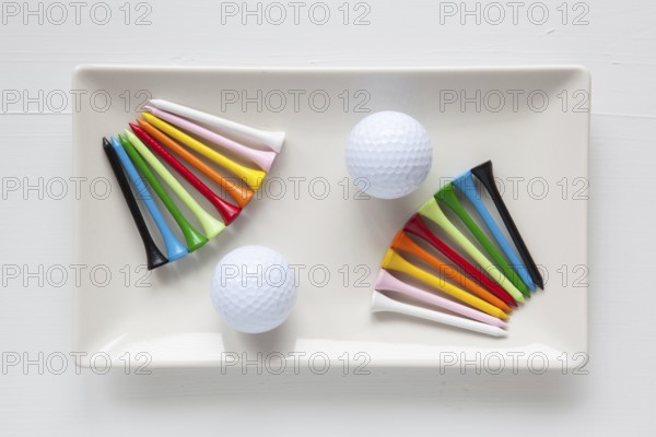 White ceramic dishes with golf balls and wooden tees on over white background, rectangle dish
