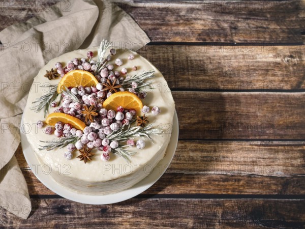 Winter homemade cake on wooden background. White cream christmas cake decored rosemary, cranberries, star anise and oranges slices. Copy space. Top view