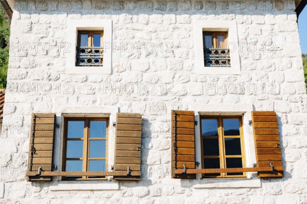 The house is white brick with large windows and wooden shutters below and small windows with metal bars above them.
