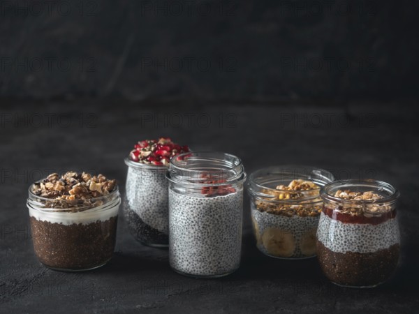 Set of chia pudding in different glass jars on dark table. Assortment of chia puding with different fruits, nuts, ingredients. Copy space for text. Superfood, detox, healthy overnight breakfast concept