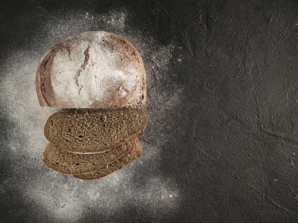 Sliced homemade sourdough rye bread with rye flour on black textured background. Top view or flat-lay. Copy space. Low key