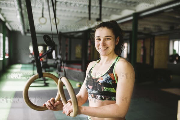 Beautiful girl doing an exercise on the gym rings in the gym. Happy and smiling
