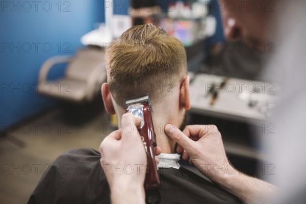 Close up shot of a man getting a trendy haircut at a hair salon. Male caucasian hairdresser serving a client. Man with a beard making haircut with a typewriter and comb