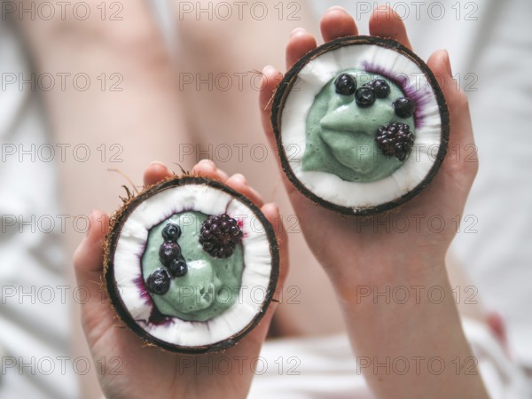 Two coconut half with smoothie or yogurt in woman hands. Blue spirulina smoothie in coconut with frozen berries. Healthy breakfast concept. Ideas and recipes for healthy vegan breakfast. Copy space
