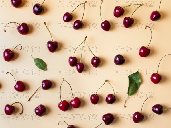 Fresh cherries scattered on yellow background. Creative fresh cherry pattern background with copy space. Top view or flat lay. Sprinkled cherry with green leaves as creative layout for food background