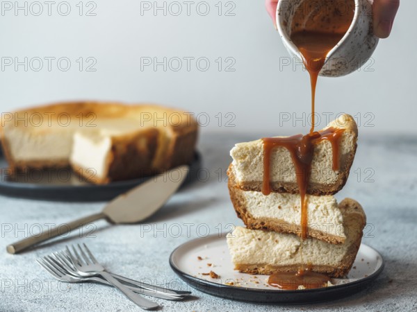 Caramel pouring on stack of three cheesekace pieces. Cheesecake with caramel on gray cement background. Copy space for text
